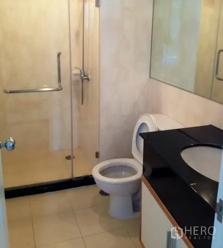 Condominium for rent in Watthana, Bangkok - Bathroom with glass-enclosed shower, vanity with black countertop, and toilet.