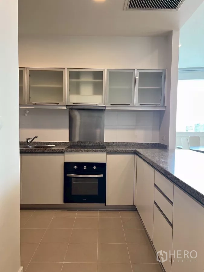 公寓 出租在Khlong Toei, Bangkok - 现代U型厨房，花岗岩台面、嵌入式烤箱与磨砂玻璃吊柜。