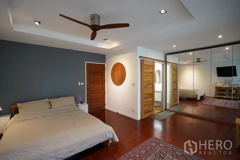 Townhouse for rent in Khlong Toei, Bangkok - Spacious master bedroom with wood floors, ceiling fan, mirrored wardrobe and en-suite access.