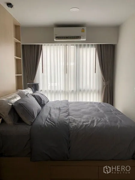 Condominium for rent or sale in Yan Nawa, Bangkok - Cozy bedroom with double bed, built-in shelving, air conditioner, and curtained window.