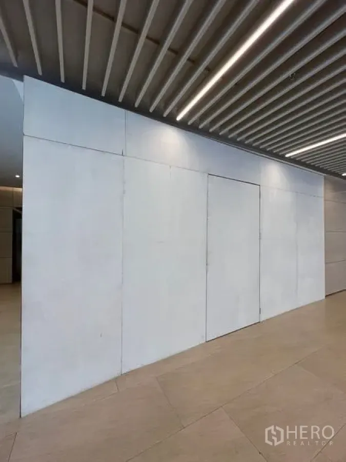 零售空间 出租在Pathum Wan, Bangkok - 关闭中的商铺门面，白色面板与门，顶部线性灯光。