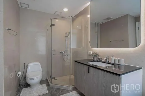 คอนโด ให้เช่าหรือขายในWatthana, Bangkok - ห้องน้ำร่วมสมัยพร้อมตู้อาบน้ำกระจก เคาน์เตอร์อ่างล้างหน้า และโถสุขภัณฑ์.