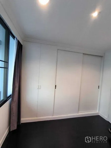 คอนโด ให้เช่าในWatthana, Bangkok - ผนังตู้เสื้อผ้าบานเลื่อนสีขาวและพื้นไม้สีเข้มในห้องนอน