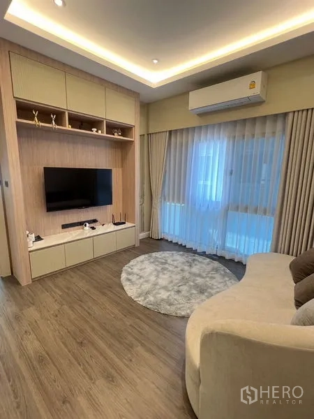 Detached House for sale in Bang Kapi, Bangkok - Upper family room with built-in TV unit, curved sofa and glass doors to a balcony.