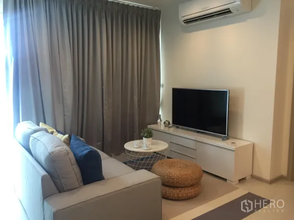 公寓 出租在Khlong Toei, Bangkok - 客厅角落，电视柜、空调与落地窗厚窗帘，圆形茶几相伴。