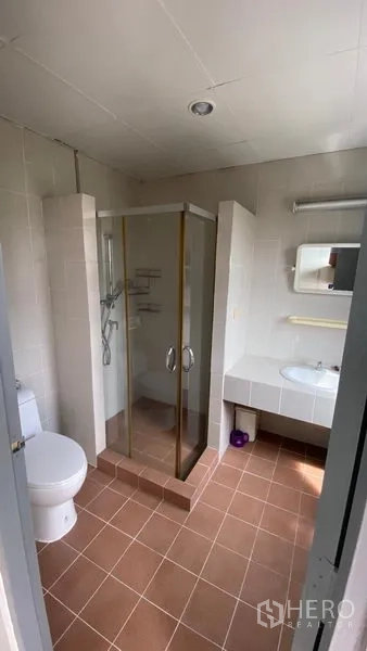 联排别墅 出租在Bang Na, Bangkok - 浴室设玻璃淋浴房、坐便和宽台面洗手盆。