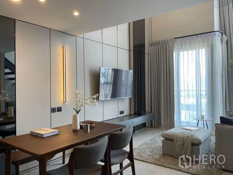 公寓 出租在Pathum Wan, Bangkok - 餐桌邻现代小厨房，灯带开放层架，后方可见楼梯与起居区。