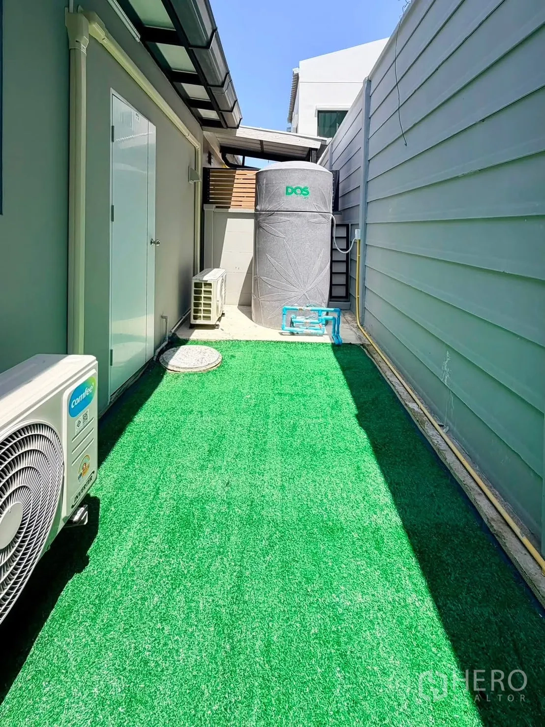 Townhouse for rent in Bang Phli, Samut Prakan - Narrow outdoor area with artificial grass, water storage tank, and air-conditioning units.
