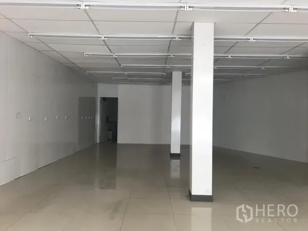 零售空间 出租在Khlong Toei, Bangkok - 开放式店铺内部，面向后方出入口，白色立柱、抛光瓷砖与吊顶线性照明。