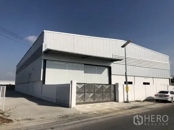 工厂 出租在Bang Phli, Samut Prakan - 金属板外立面的现代工厂，屋顶高挑，配大卷帘门与金属大门，混凝土车道与路灯一应俱全。