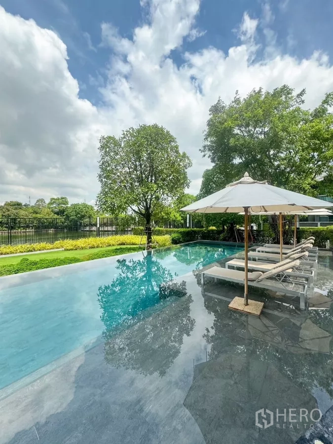 Detached House for rent or sale in Bueng Kum, Bangkok - Resort-style communal swimming pool with sun loungers, umbrellas and lush greenery.