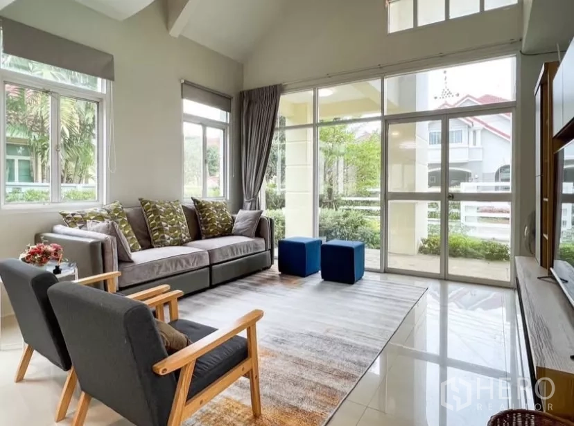 Detached House for rent or sale in Prawet, Bangkok - Living area with floor-to-ceiling glass opening to the porch and greenery.