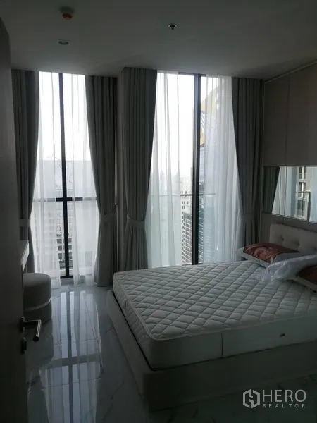 คอนโด ให้เช่าในPathum Wan, Bangkok - ห้องนอนมุมอาคาร หน้าต่างสูง วิวเมือง และเตียงควีนพร้อมม่านสีอ่อน