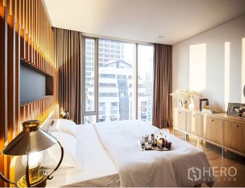 公寓 出租在Bang Rak, Bangkok - 采光明亮的卧室，落地窗眺望城市天际线与木质装饰墙。