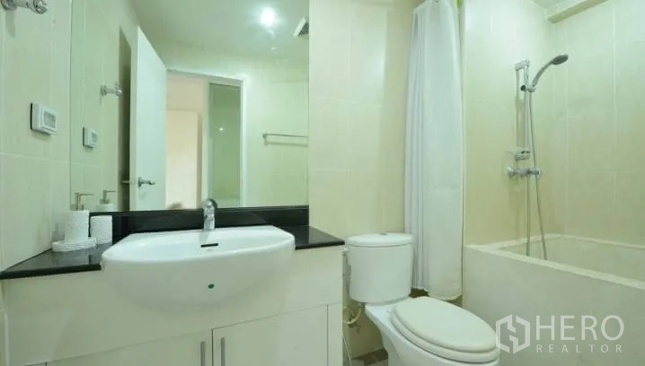 Condominium for rent in Watthana, Bangkok - Clean bathroom with vanity, large mirror, toilet and bathtub with shower curtain.
