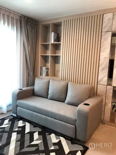 คอนโด ให้เช่า - มุมพักผ่อนด้วยโซฟาสีเทา ผนังลายซี่ไม้ พร้อมชั้นบิลท์อินข้างหน้าต่าง