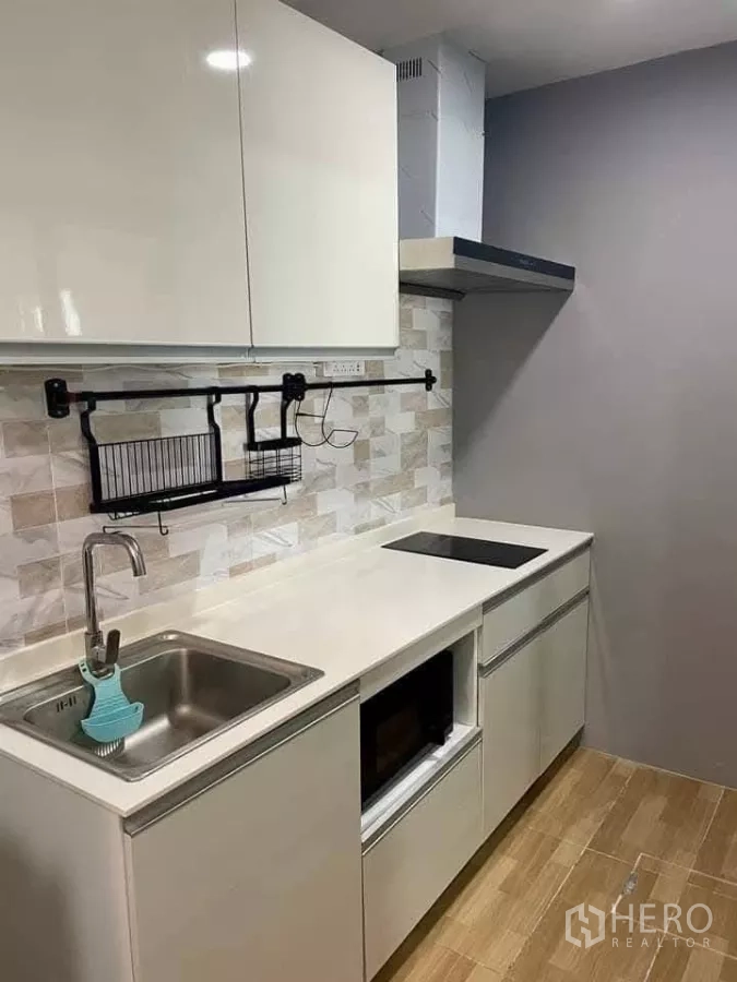 Townhouse for rent in Bang Phli, Samut Prakan - Compact kitchen with white cabinets, sink, induction hob and tiled backsplash.