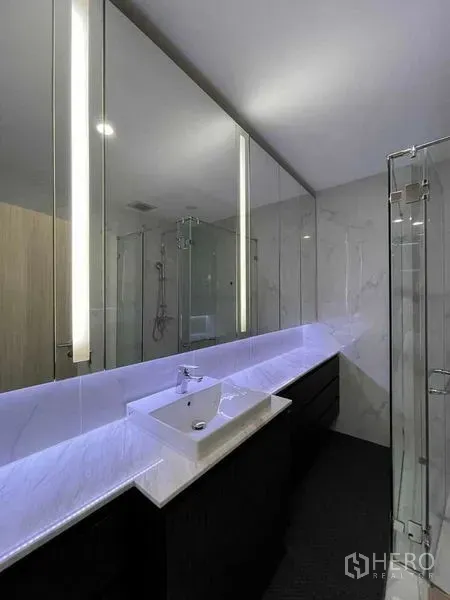 Condominium for rent in Pathum Wan, Bangkok - Modern bathroom with long marble countertop, backlit mirror and glass shower.