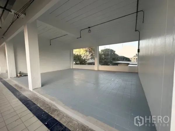 พื้นที่ขายปลีก ให้เช่า - พื้นที่ค้าปลีกเปิดโล่ง ผนังสีขาว พื้นกระเบื้องสีเทา เพดานสูง และหน้าต่างบานใหญ่เห็นวิวต้นไม้และเมือง