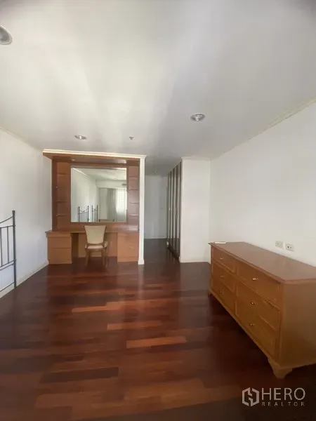 Condominium for rent or sale in Watthana, Bangkok - Bedroom with built-in dressing table, large mirror, wooden dresser and polished floors.