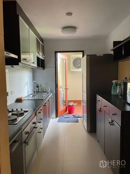 Condominium for rent in Watthana, Bangkok - Galley kitchen with dark cabinetry, stainless countertop and access to a utility balcony.