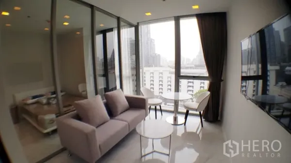 Condominium for rent in Watthana, Bangkok - Bright living room in a 1-bedroom condo with floor-to-ceiling windows, city view, glass-partitioned bedroom and wall-mounted TV in Watthana, Bangkok.