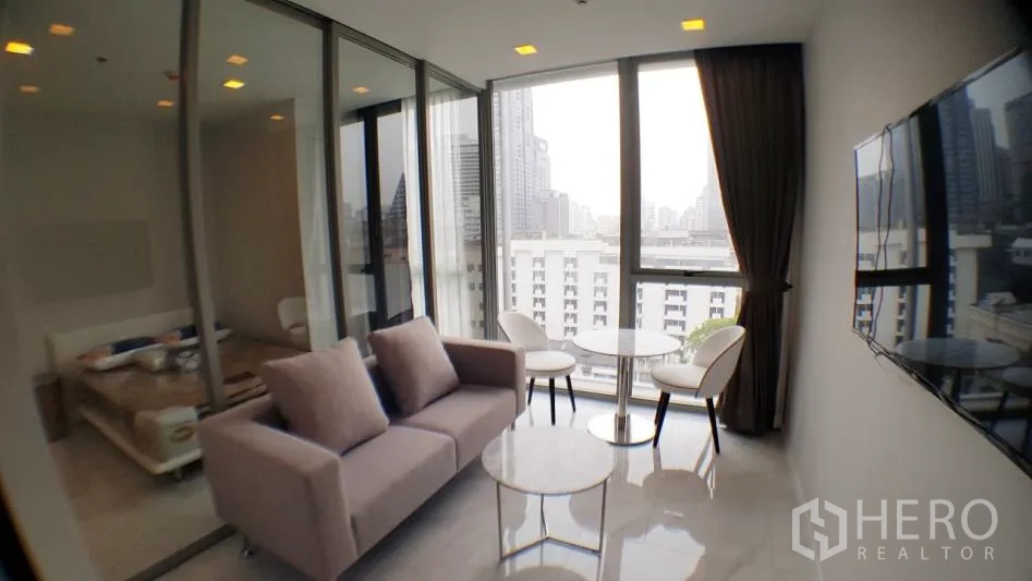Condominium for rent in Watthana, Bangkok - Bright living room in a 1-bedroom condo with floor-to-ceiling windows, city view, glass-partitioned bedroom and wall-mounted TV in Watthana, Bangkok.
