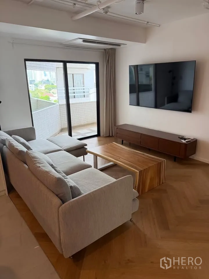 Condominium for rent in Watthana, Bangkok - Sofa facing wall-mounted TV with balcony access beyond.