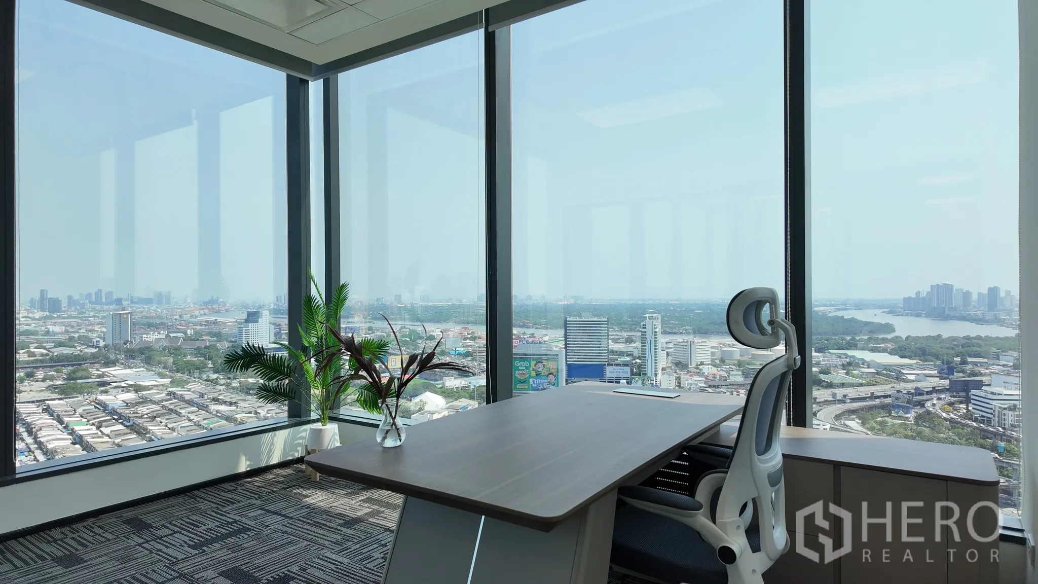 Office Space for rent in Khlong Toei, Bangkok - Corner office with wraparound windows, ergonomic chair, and distant cityscape.