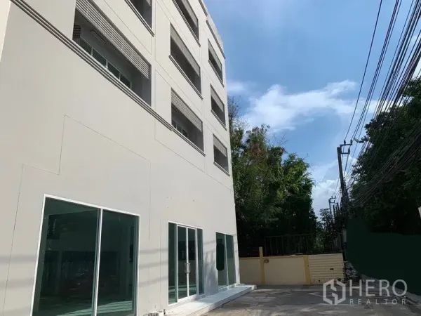 办公空间 出租在Huai Khwang, Bangkok - 办公楼侧立面，玻璃门临静巷，沿街电线与树木可见。