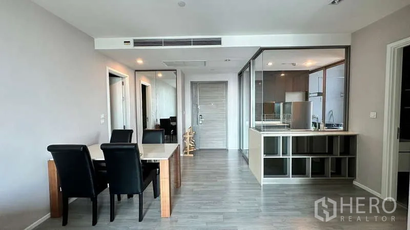 Condominium for rent - Open-plan space featuring a dining table and a glass-partitioned kitchen with built-in cabinets and an entry door.