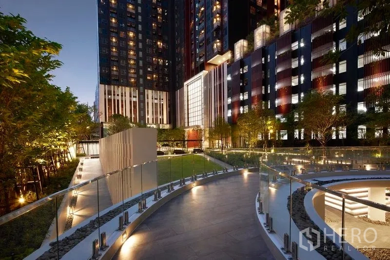 公寓 出售在Ratchathewi, Bangkok - 夜色中景观花园与弧形步道，毗邻现代高层公寓。