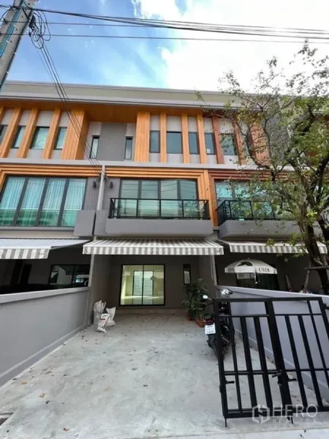 Townhouse for rent - Modern three-storey townhouse facade with gated driveway, striped awnings and a balcony in Prawet.