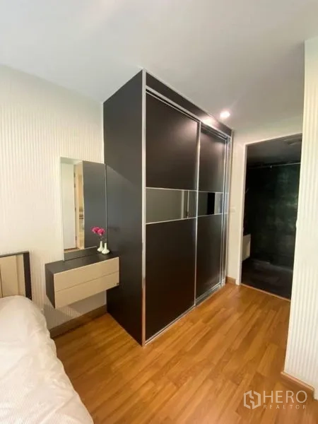 Condominium for rent in Watthana, Bangkok - Sliding-door wardrobe beside a compact dressing table and access to a dark-tiled bathroom.