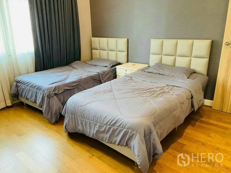 Condominium for rent in Watthana, Bangkok - Second bedroom with two single beds, padded headboards, and wood floors.