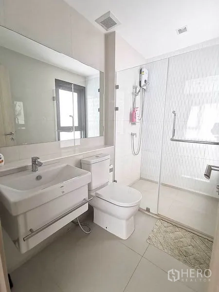 Condominium for rent in Pathum Wan, Bangkok - Second bathroom with large mirror, glass-enclosed shower and window.