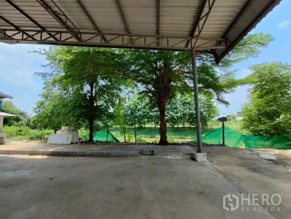 Factory for rent in Mueang Chachoengsao, Chachoengsao - Shaded canopy and open yard facing green trees along the property edge.