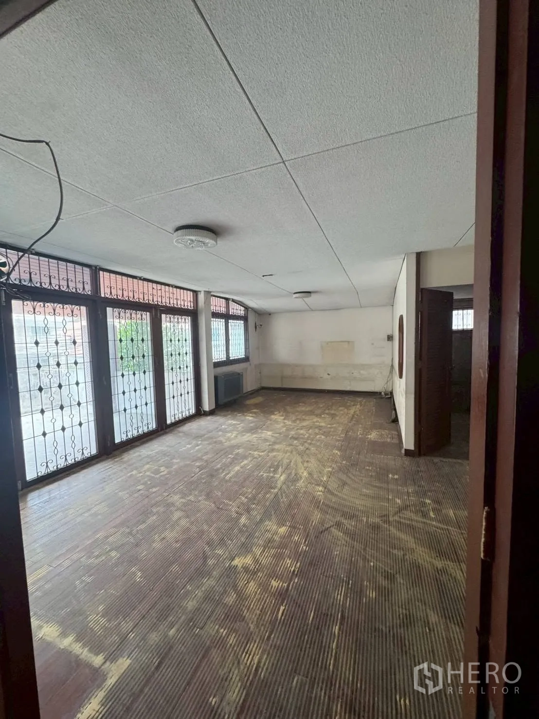 Detached House for rent or sale in Watthana, Bangkok - Spacious room with worn wood flooring and metal-grilled glass doors.