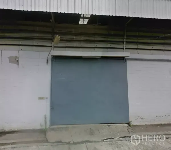 คลังสินค้า ให้เช่าในBang Phli, Samut Prakan - ด้านหน้าโกดังอุตสาหกรรมในบางพลี พร้อมประตูบานเลื่อนเหล็กขนาดใหญ่ หลังคาเมทัลชีท และทางลาดคอนกรีตสำหรับขนถ่ายสินค้า