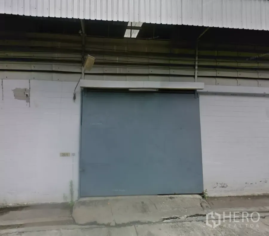 คลังสินค้า ให้เช่าในBang Phli, Samut Prakan - ด้านหน้าโกดังอุตสาหกรรมในบางพลี พร้อมประตูบานเลื่อนเหล็กขนาดใหญ่ หลังคาเมทัลชีท และทางลาดคอนกรีตสำหรับขนถ่ายสินค้า