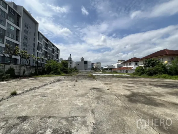 Land for sale in Bang Kapi, Bangkok - Vacant concrete land parcel bordered by condos on the left and houses on the right in Bang Kapi.