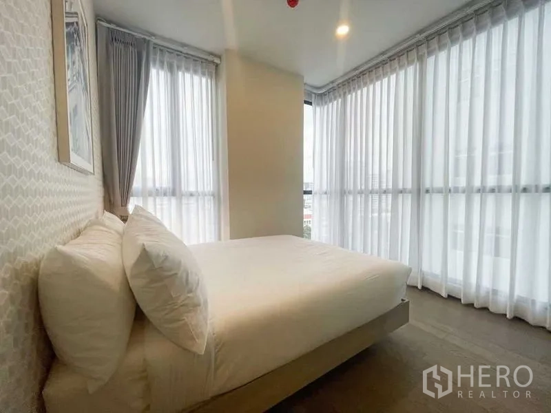 Condominium for rent in Ratchathewi, Bangkok - Corner bedroom with wraparound floor-to-ceiling windows and white drapes providing abundant natural light.