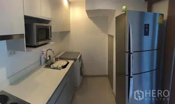 公寓 出租在Phra Khanong, Bangkok - 现代一字型厨房，白色橱柜，不锈钢冰箱、微波炉与洗衣机。