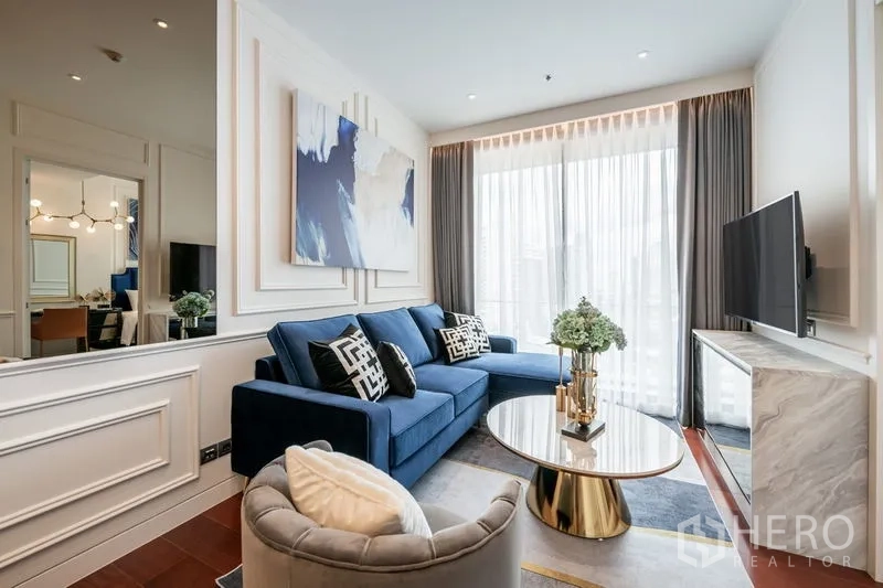 คอนโด ให้เช่าในWatthana, Bangkok - ห้องนั่งเล่นโซฟาสีน้ำเงิน โต๊ะกลางหินอ่อน และทีวีติดผนังข้างประตูกระจกออกระเบียง