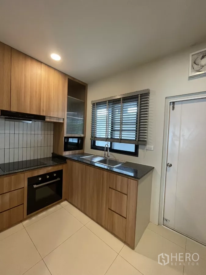 Detached House for rent in Bang Phli, Samut Prakan - Kitchen angle showing sink under window, cabinetry and built-in oven.