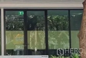 Retail Space for rent in Khlong Toei, Bangkok - Close-up of shopfront with black-framed glass doors, an emergency exit sign overhead, and a tree-shaded frontage.