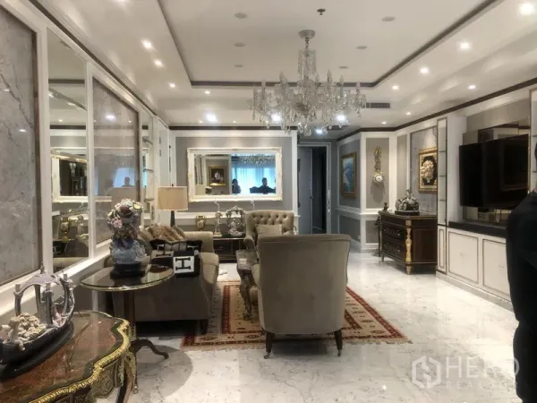 公寓 出售在Watthana, Bangkok - 客厅铺大理石地面，搭配纽扣沙发、水晶吊灯、镜面墙与经典柜体。