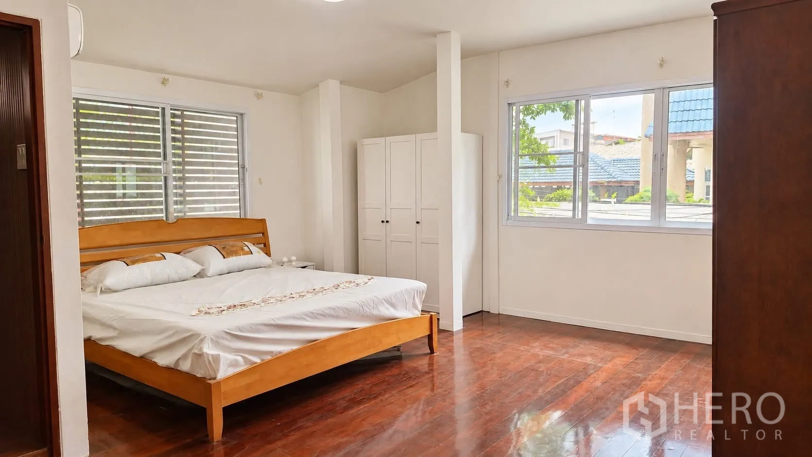 Detached House for rent in Khlong Toei, Bangkok - Spacious bedroom with wooden bed frame, wardrobes, and wide windows.