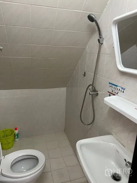 Townhouse for rent in Khlong Toei, Bangkok - Bathroom with shower, toilet and sink beneath a sloped tiled ceiling.