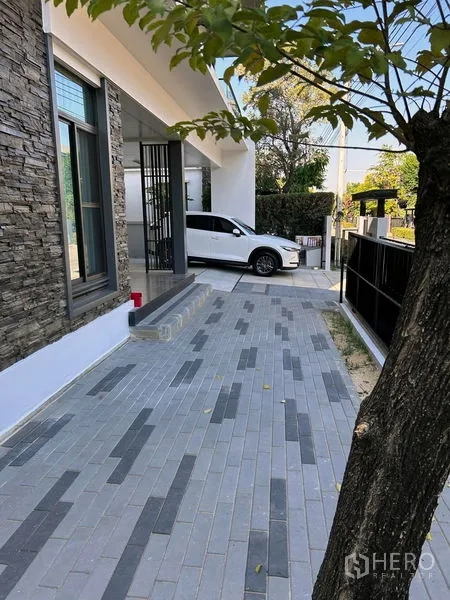 Detached House for rent or sale in Prawet, Bangkok - Driveway with gray pavers beside stone-clad exterior wall and parked car.